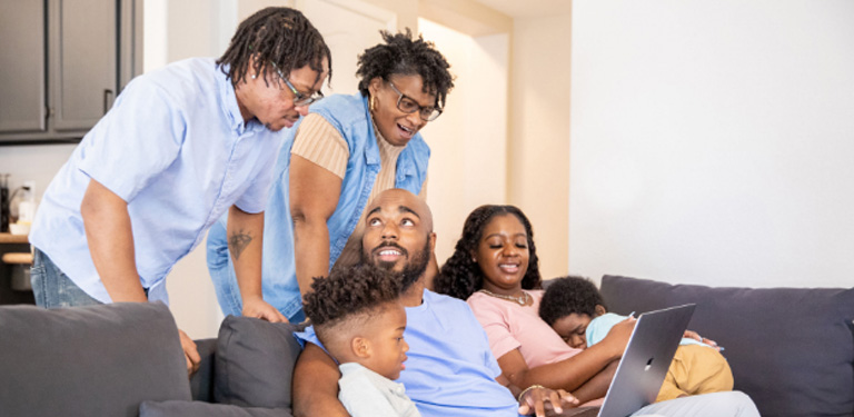 Image of an immediate family gathering with their extended family members looking at a laptop computer